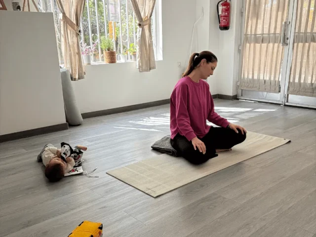 Mamá meditando sobre la esterilla en el centro de Mamá Yoguini mientras su bebé juega a su lado