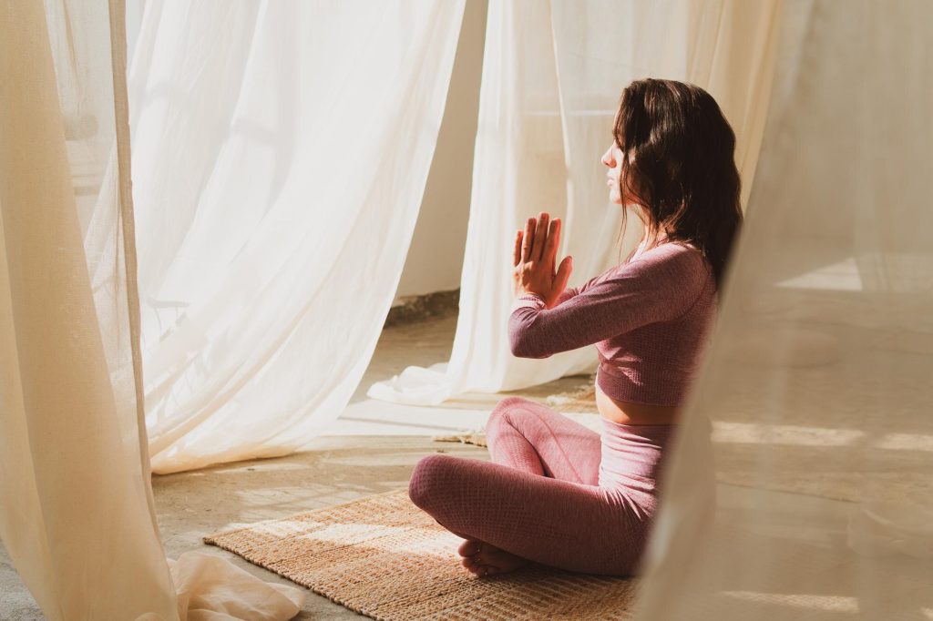 Mujer practicando yoga junto a una ventana con cortinas de luz cálida