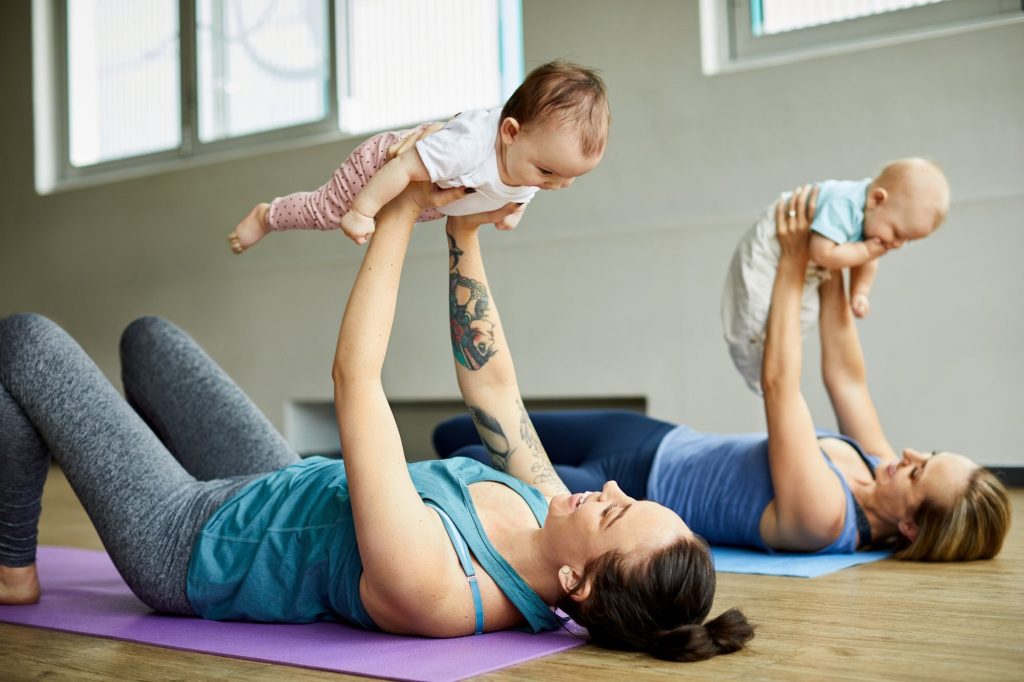 Dos madres haciendo yoga posparto con sus bebés en brazos